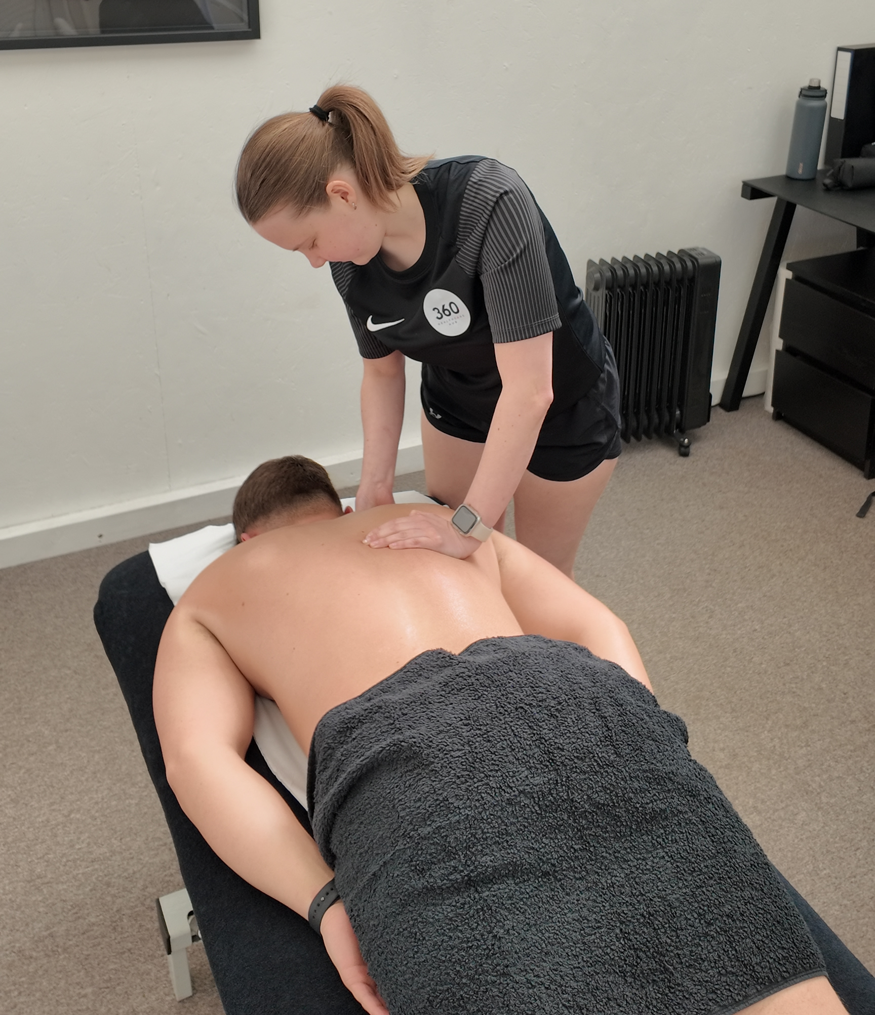 A therapist massaging a client’s upper back as they lie face down on a treatment couch