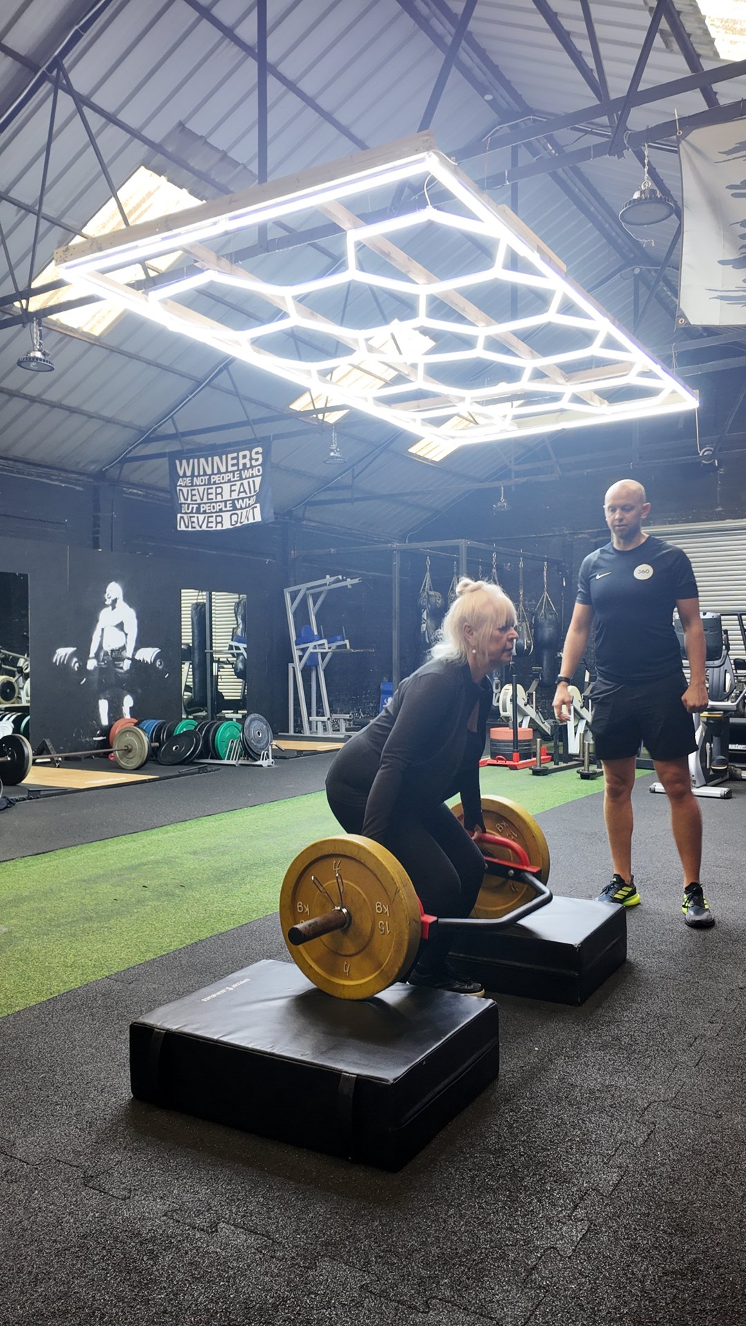 A client lifting a trap bar from blocks with Ben supervising at 360 Healthcare Hub